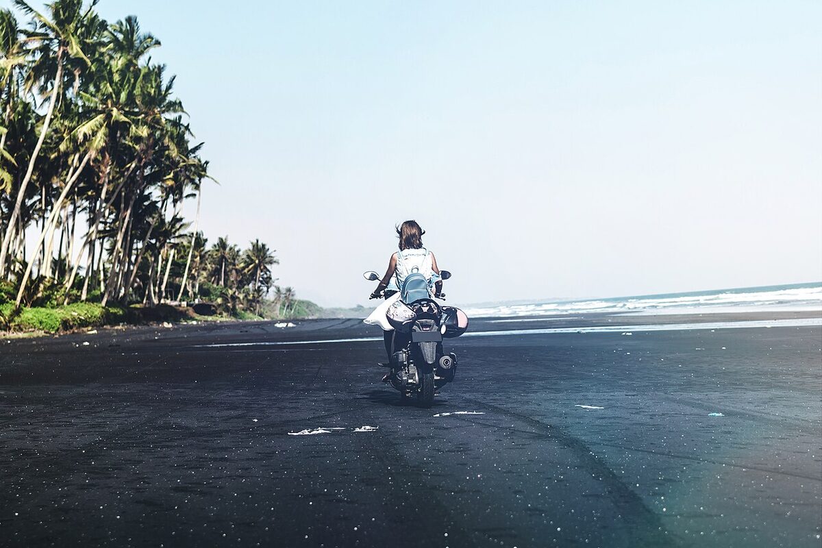 Pengendara skuter di pantai berpasir hitam, Bali